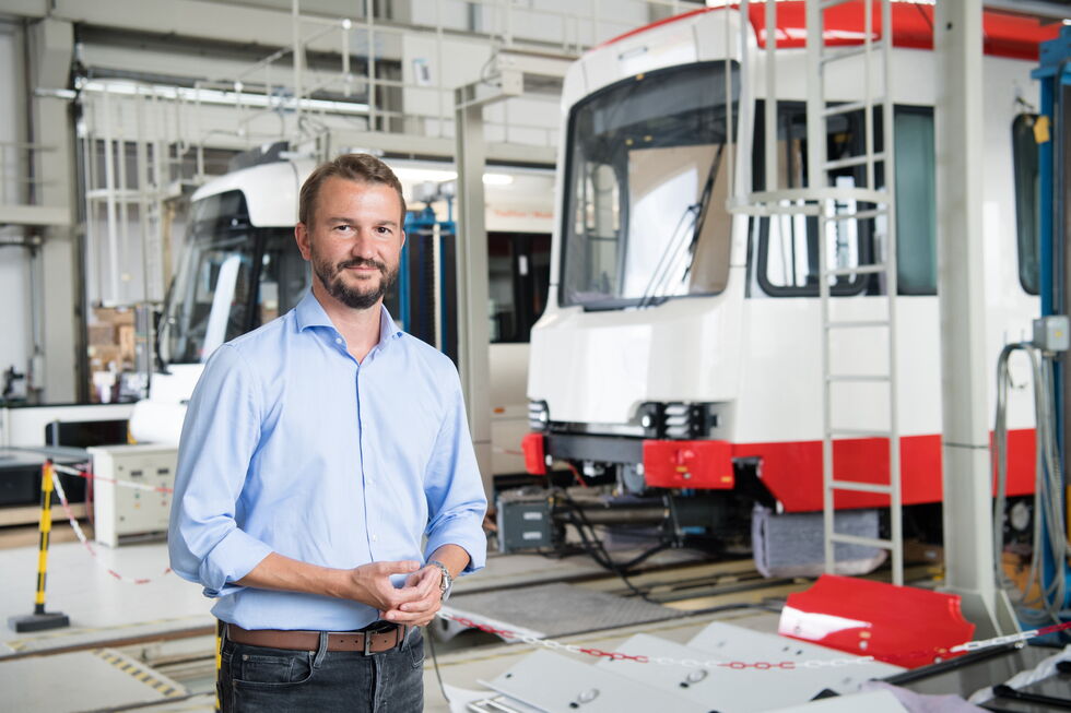 Samuel Kermelk steht vor Straßenbahnen in einer Produktionshalle