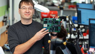 Andreas Ullmann zeigt vor Löt-Arbeitsplätzen in seinem Zittauer Betrieb ein Versuchsgerät für die Zentralelektronik im Auto.  ECU.de repariert elektronische Kfz-Bauteile, an die sich viele andere nicht heranwagen.